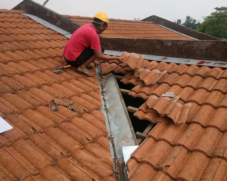 Tukang ASATURA membongkar dan menata ulang genteng di sekitar talang jurai