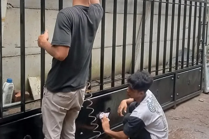 Dua tukang ASATURA mengecat pagar besi hitam di Jakarta Timur