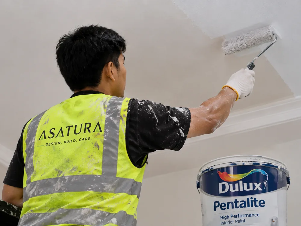 Tukang ASATURA mengecat plafon gypsum menggunakan roller bergagang panjang